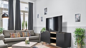 Uma sala de estar moderna com um sofá cinza, almofadas coloridas, uma televisão de tela plana, um móvel de entretenimento preto e um tapete azul.