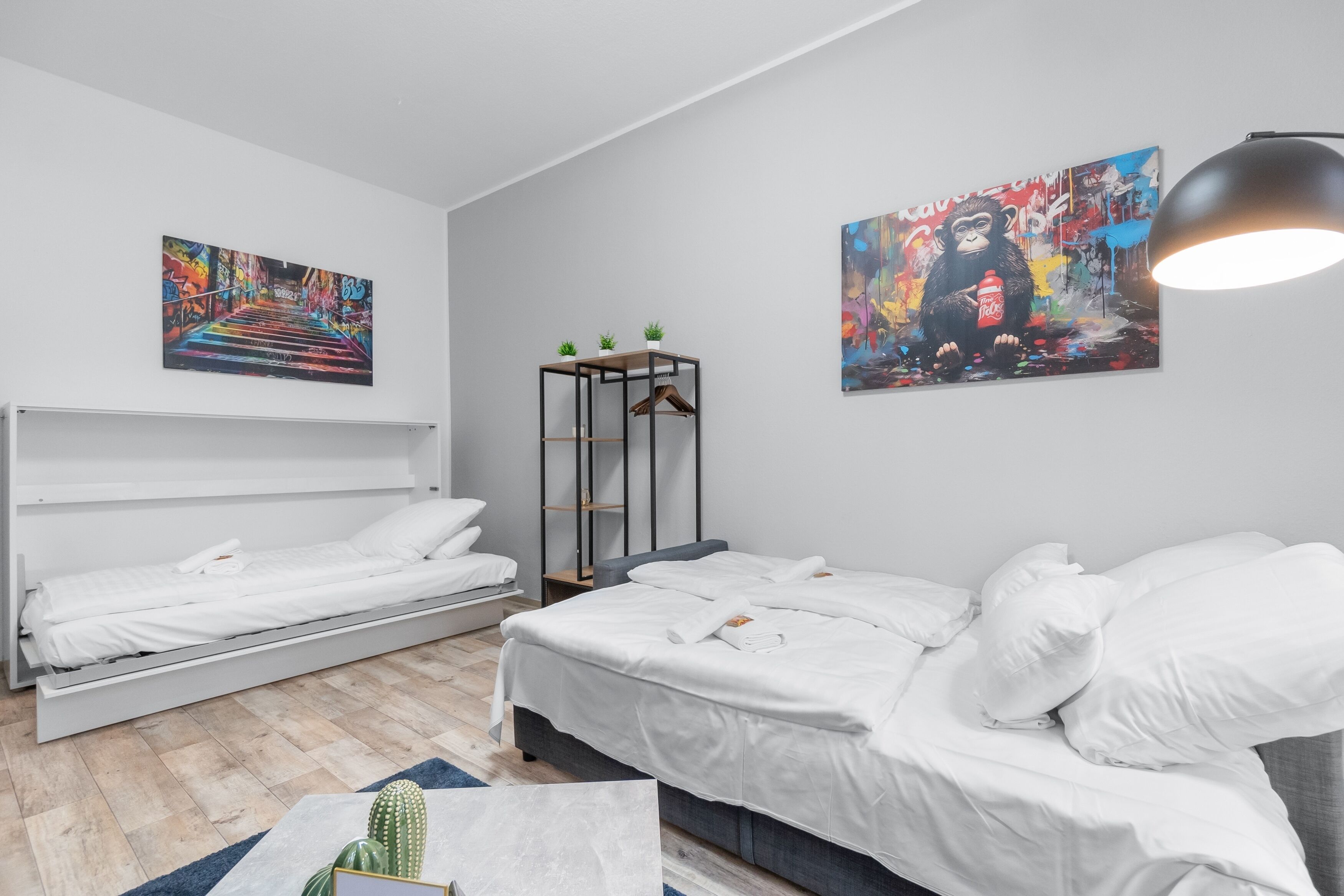 Ein modernes Hotelzimmer mit zwei Einzelbetten, einem kleinen Tisch mit Pflanzen und zwei farbenfrohen Bildern an den Wänden.