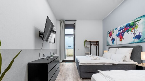 Quarto de hotel moderno com cama grande, televisão presa à parede, obra de arte com um mapa-múndi e varanda com vista.