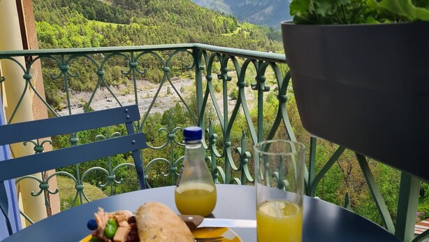 Una taula amb un entrepà, una ampolla de suc i un got de suc en un balcó amb vista a la muntanya.