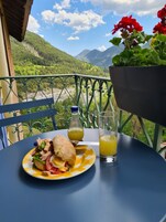 Uma mesa com um sanduíche, uma garrafa de suco e um copo de suco numa varanda com vista para as montanhas.