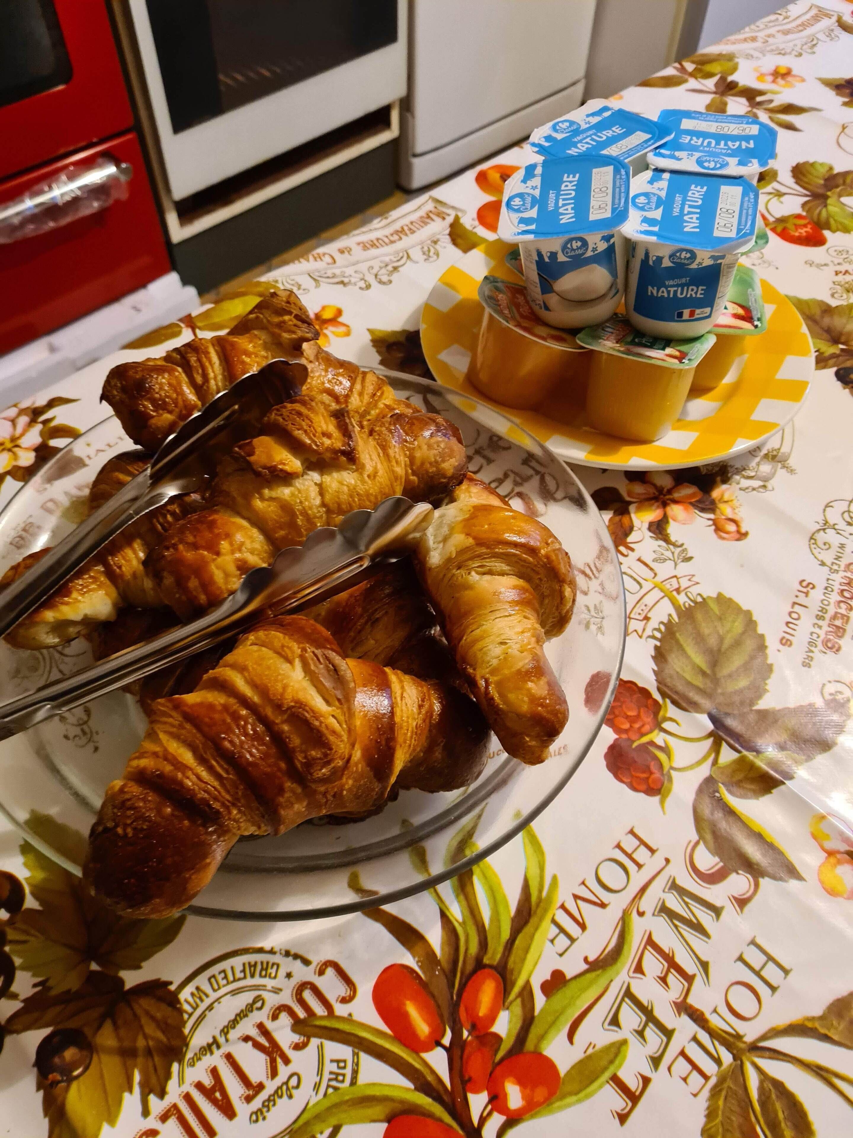 A plate of croissants on a floral tablecloth with a plate of fruit and a container of yogurt.