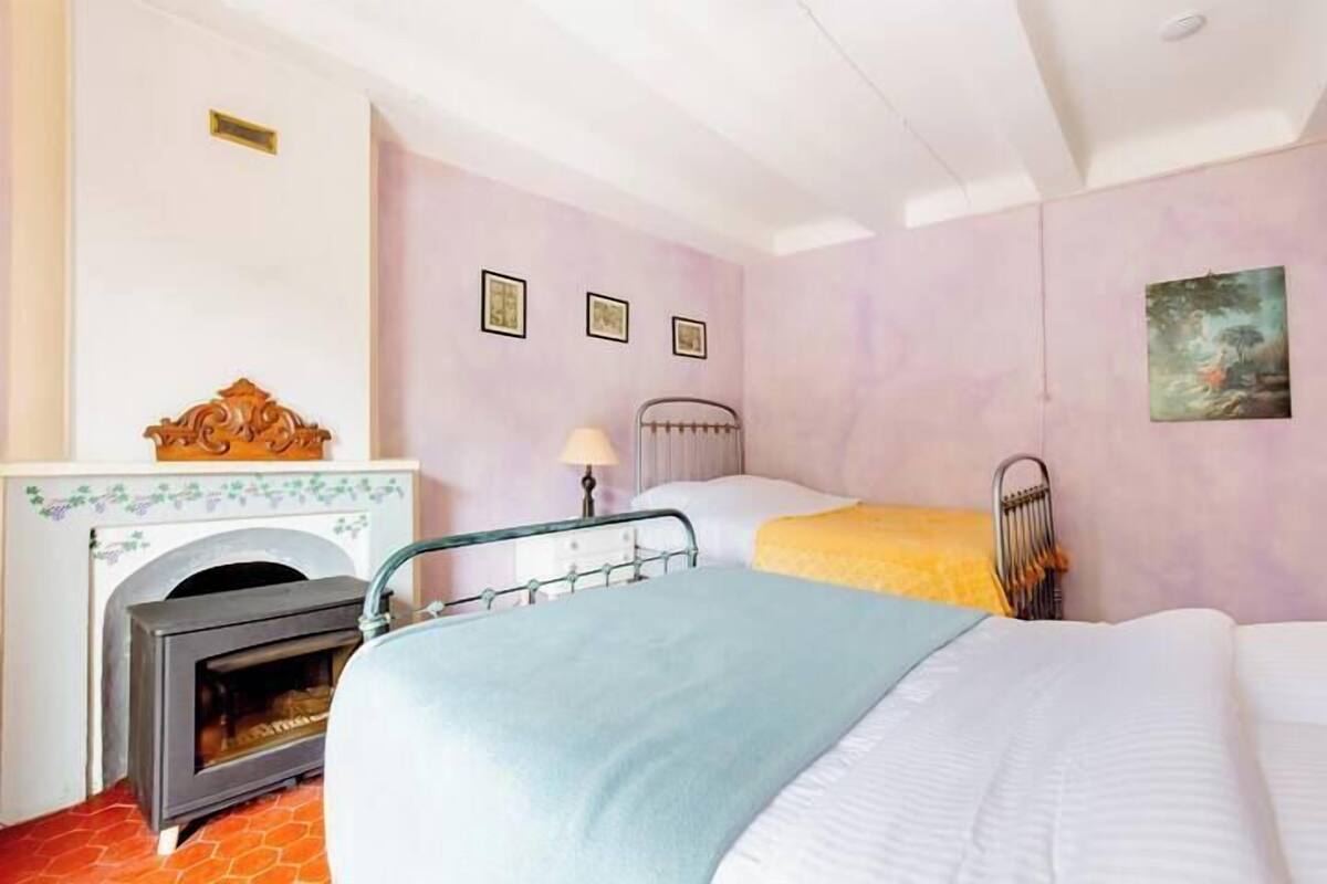 A bedroom with a fireplace, two beds, a nightstand, and a wall-mounted picture.