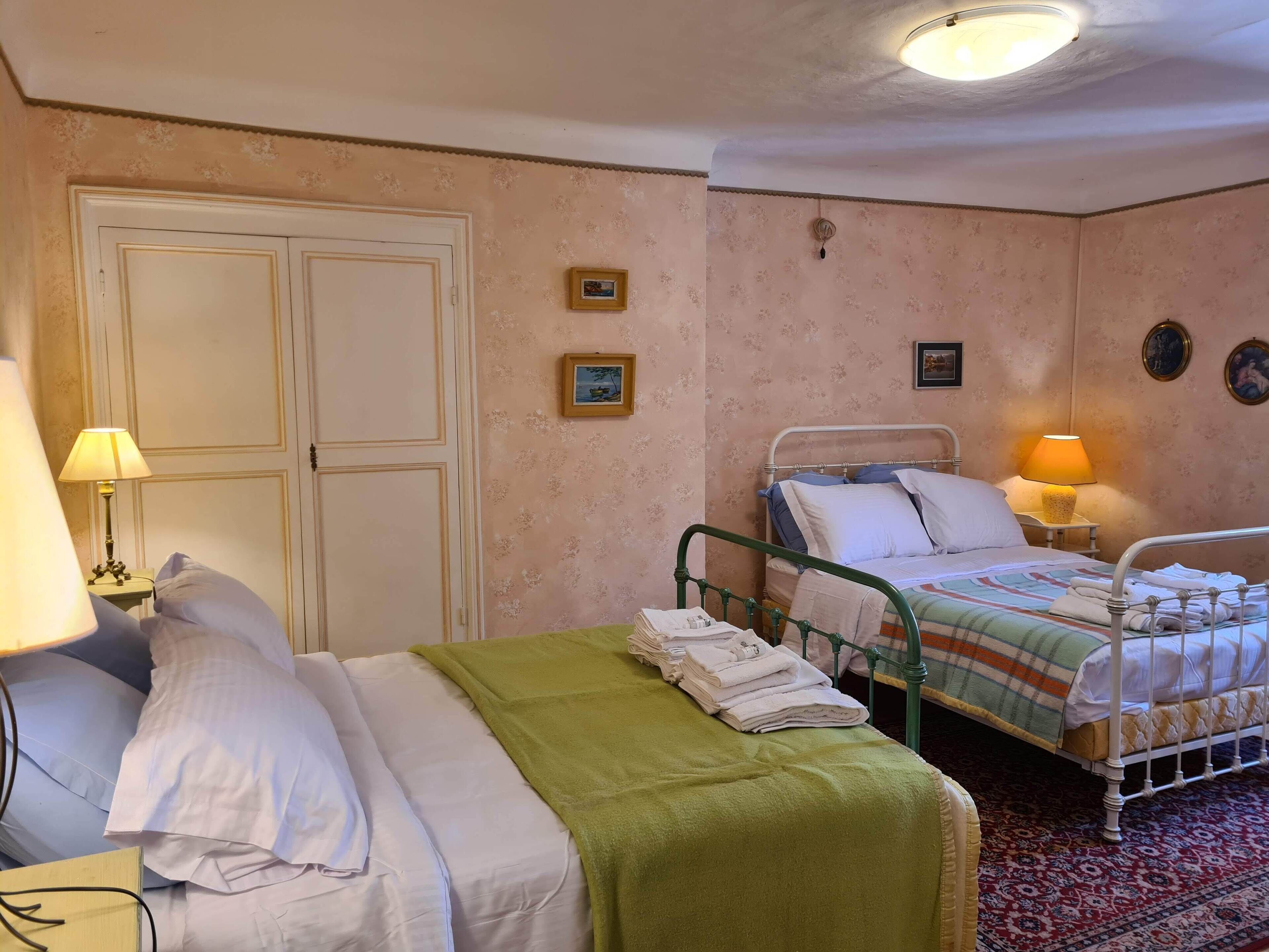 A hotel room with two beds, a green blanket on one bed, a folded towel on the other, and a red patterned rug.