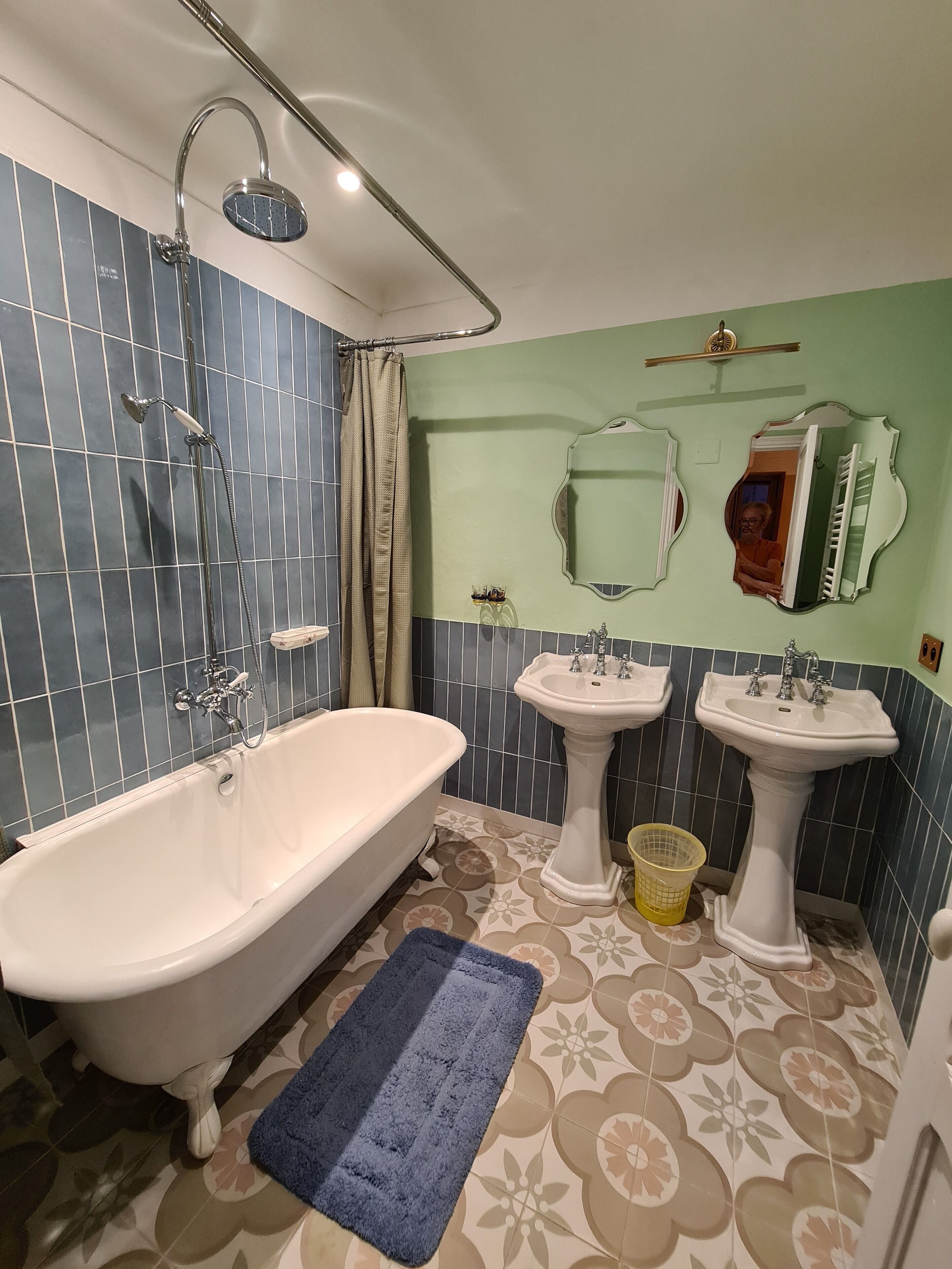 Um banheiro com uma banheira de pé, duas pias em pedestal, um chuveiro e um espelho com moldura decorativa.