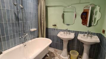 Um banheiro com uma banheira de pé, duas pias em pedestal, um chuveiro e um espelho com moldura decorativa.