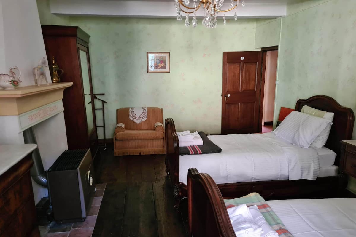 A room with a bed, a chair, a wooden wardrobe, a small table, and a chandelier.