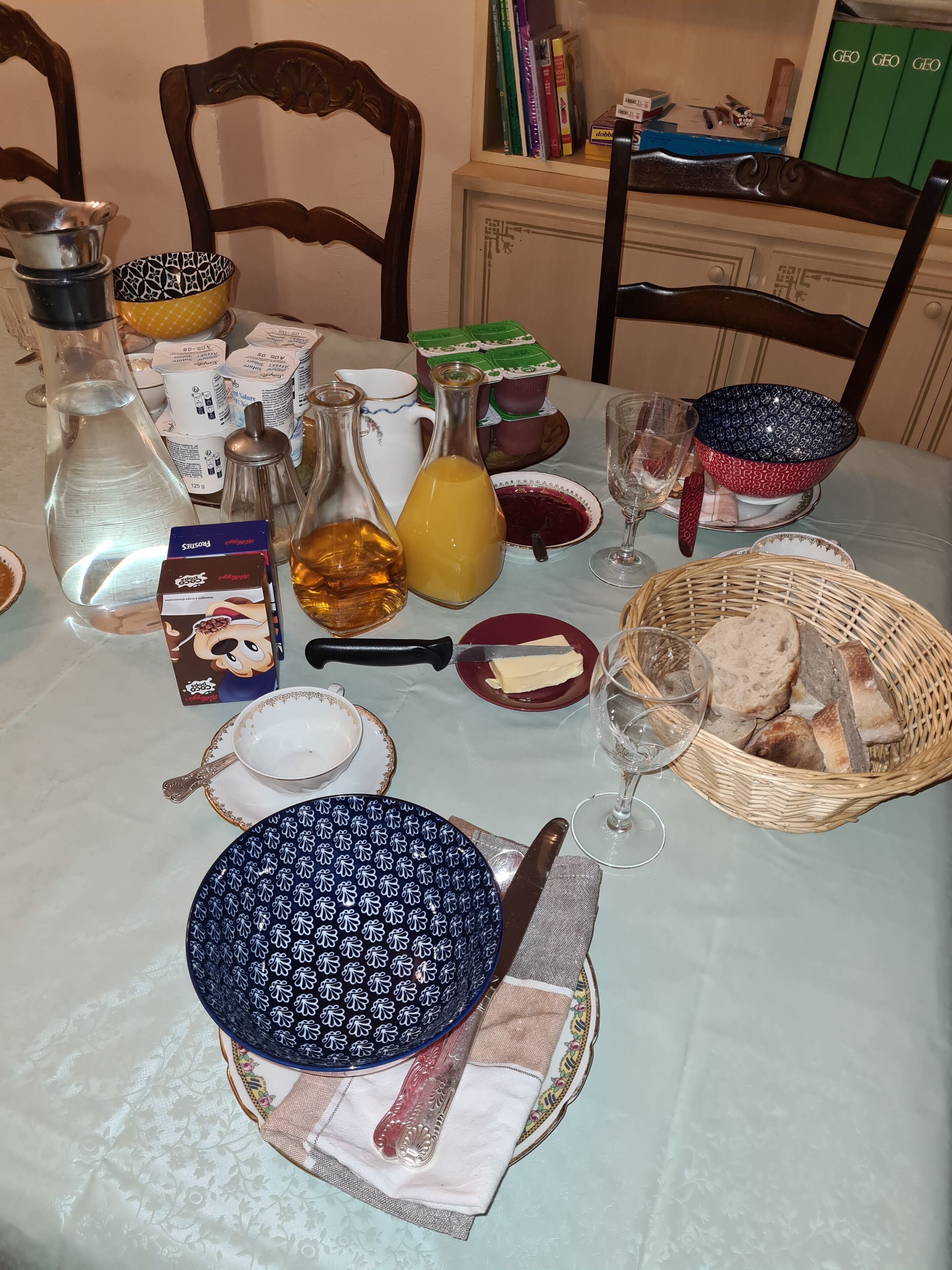 Mesa de jantar posta com diversos pratos, copos e uma cesta de pão.