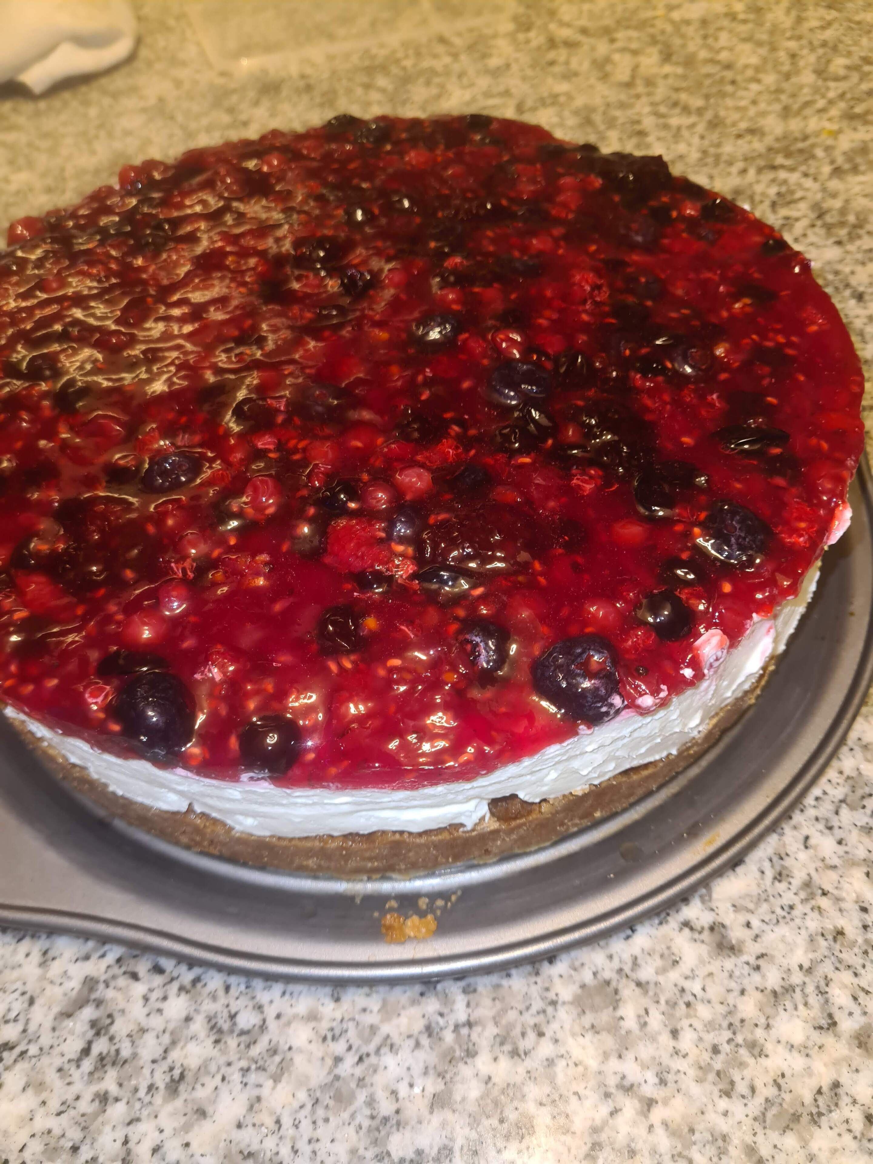 A round cake with a red fruit topping on a metal cake stand.