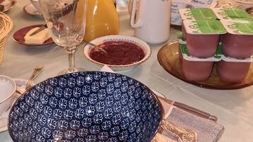 A dining table set with various items including a patterned bowl, a glass pitcher, a jug of orange juice, a white mug, and several packaged food items.