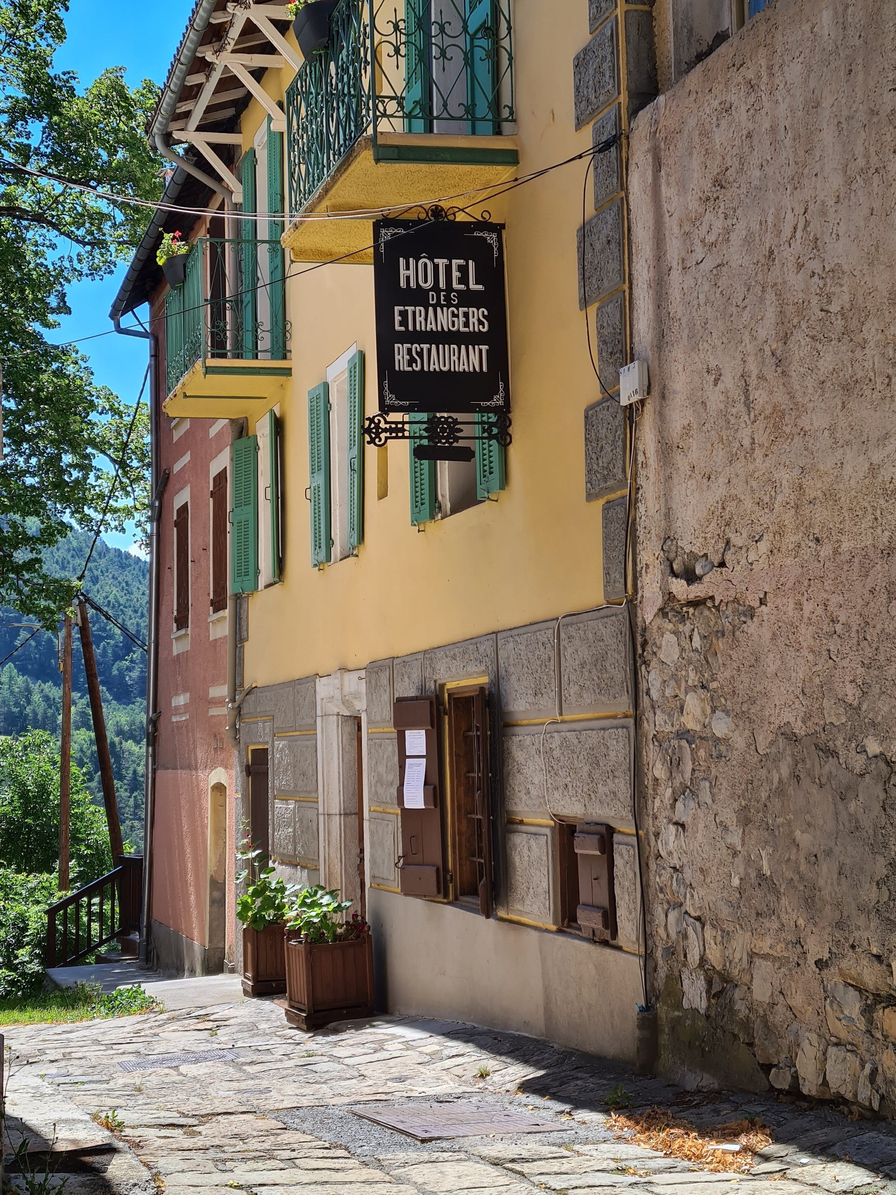 A building with a sign reading "HOTEL DES ETRANGERS RESTAURANT" and a stone staircase leading to the entrance.