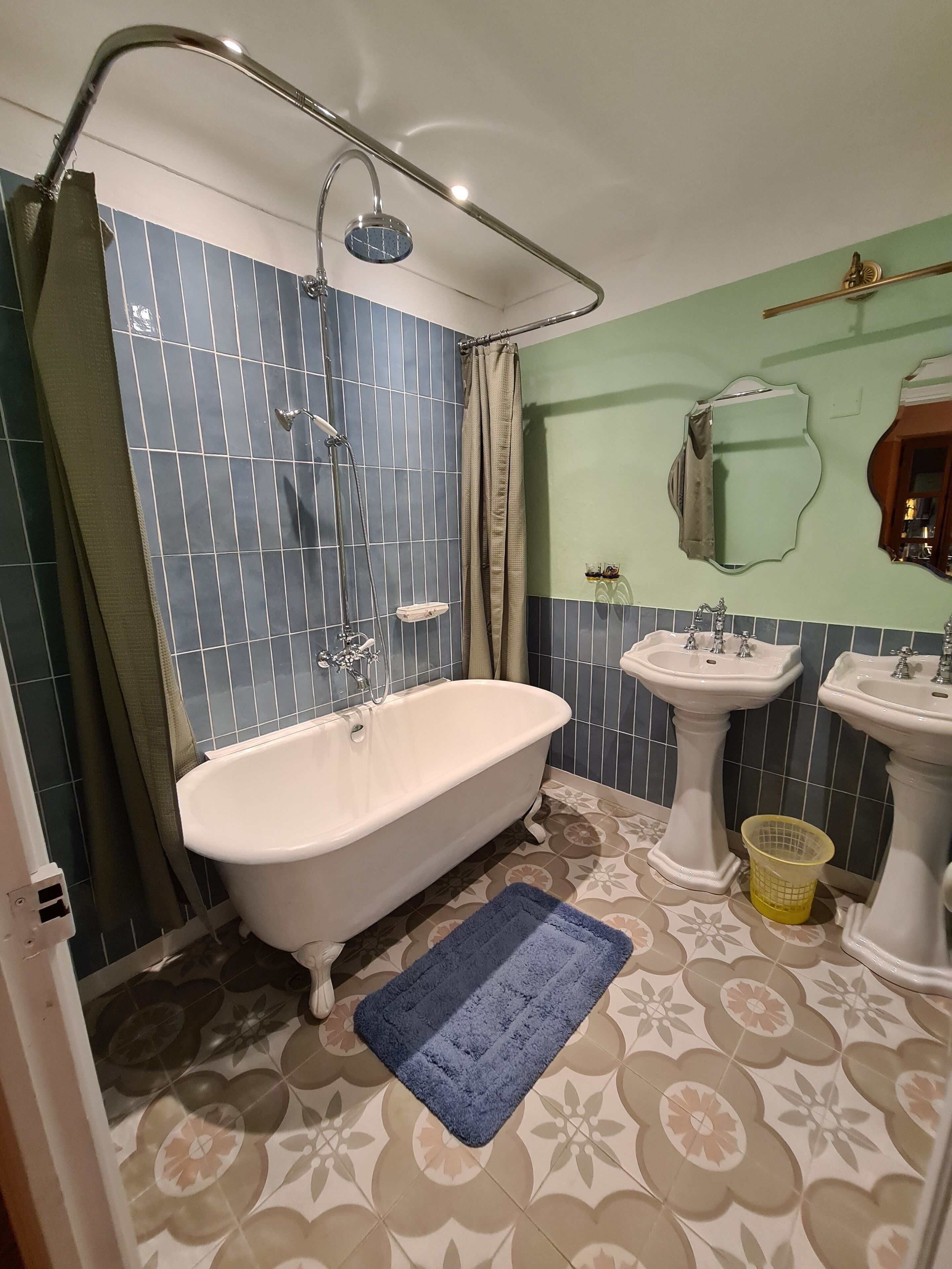 Une salle de bain avec une baignoire sur pieds, deux lavabos sur colonne, une pomme de douche et un carrelage décoratif.