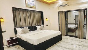 A hotel room with a bed, a desk, a mirror, and a sliding door. - Hotel Sahara Residency (Nashik)