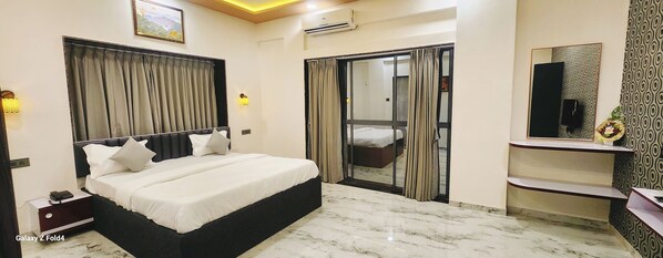 A hotel room with a bed, a desk, a mirror, and a sliding door. - Hotel Sahara Residency (Nashik)