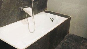 A modern bathroom with a freestanding bathtub, dark marble walls, and a towel rack. - Hotel Sahara Residency (Nashik)