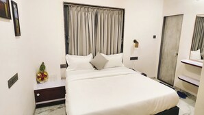 A neatly arranged hotel room with a large bed, a bedside table with a vase of flowers, a mirror, and a door with a handle. - Hotel Sahara Residency (Nashik)
