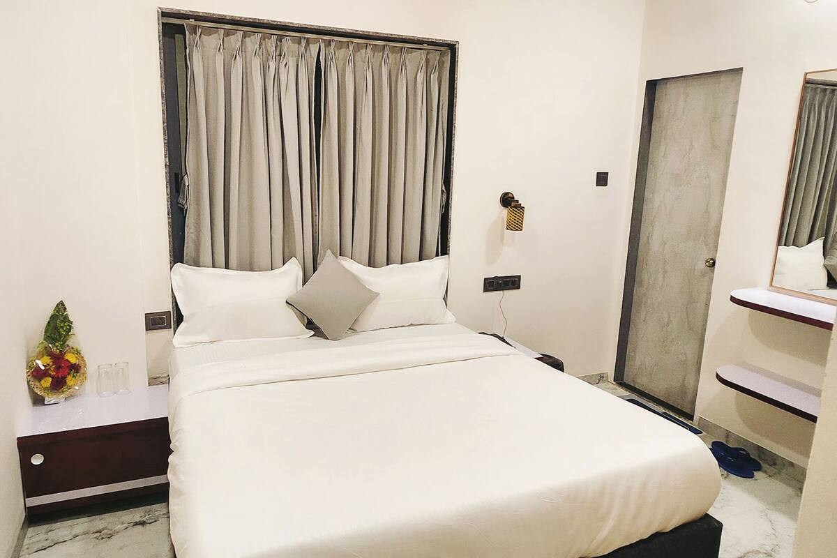 A neatly arranged hotel room with a large bed, a bedside table with a vase of flowers, a mirror, and a door with a handle.