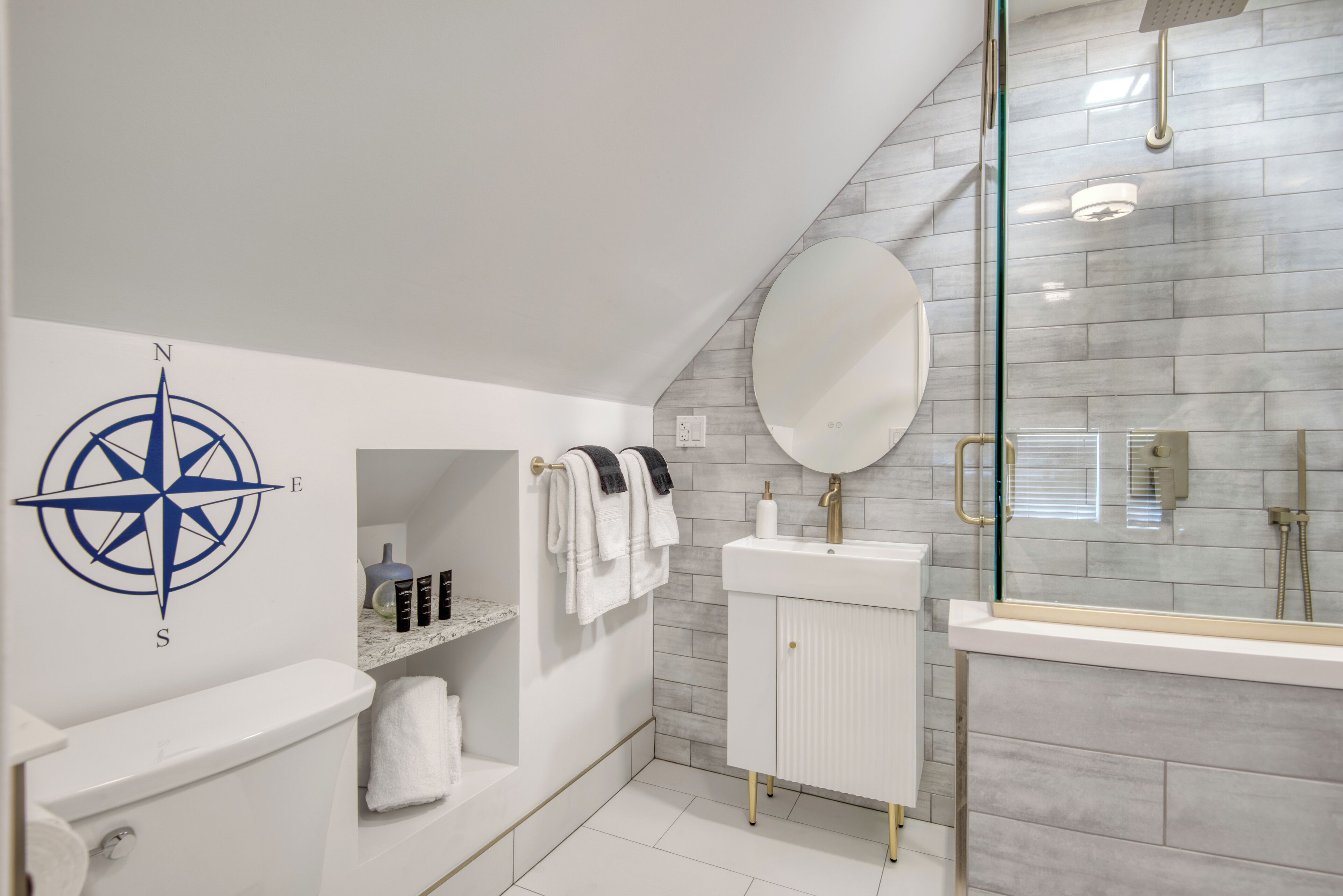 A modern bathroom with a white toilet, a sink with a round mirror, and a glass shower enclosure.