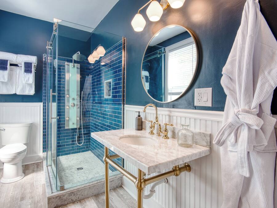 A bathroom with a glass-enclosed shower, a white toilet, a sink with gold fixtures, and a round mirror.
