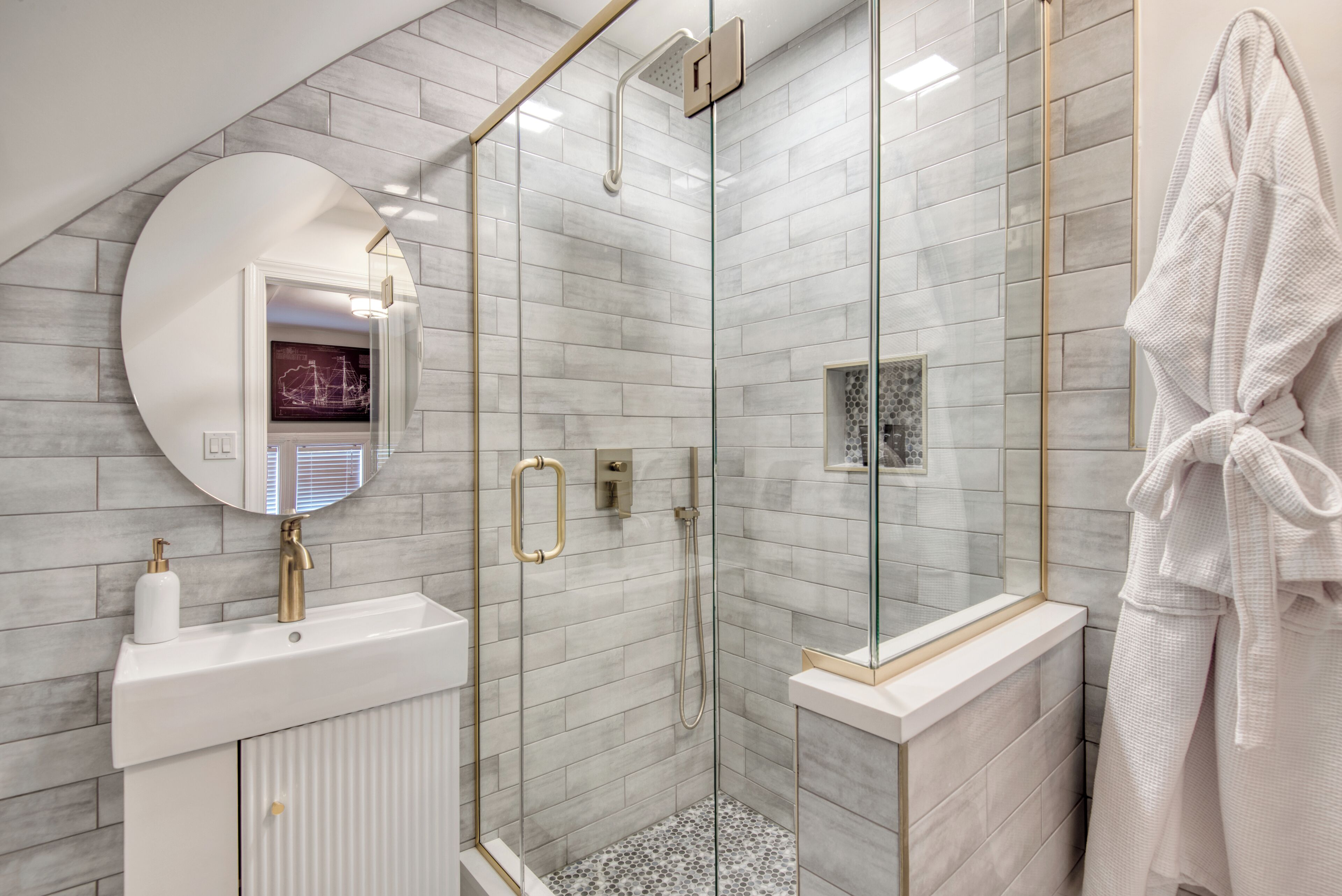 Ein modernes Badezimmer mit einer gläsernen Duschkabine, einem weißen Waschbecken mit goldfarbenen Armaturen und einem großen Spiegel.