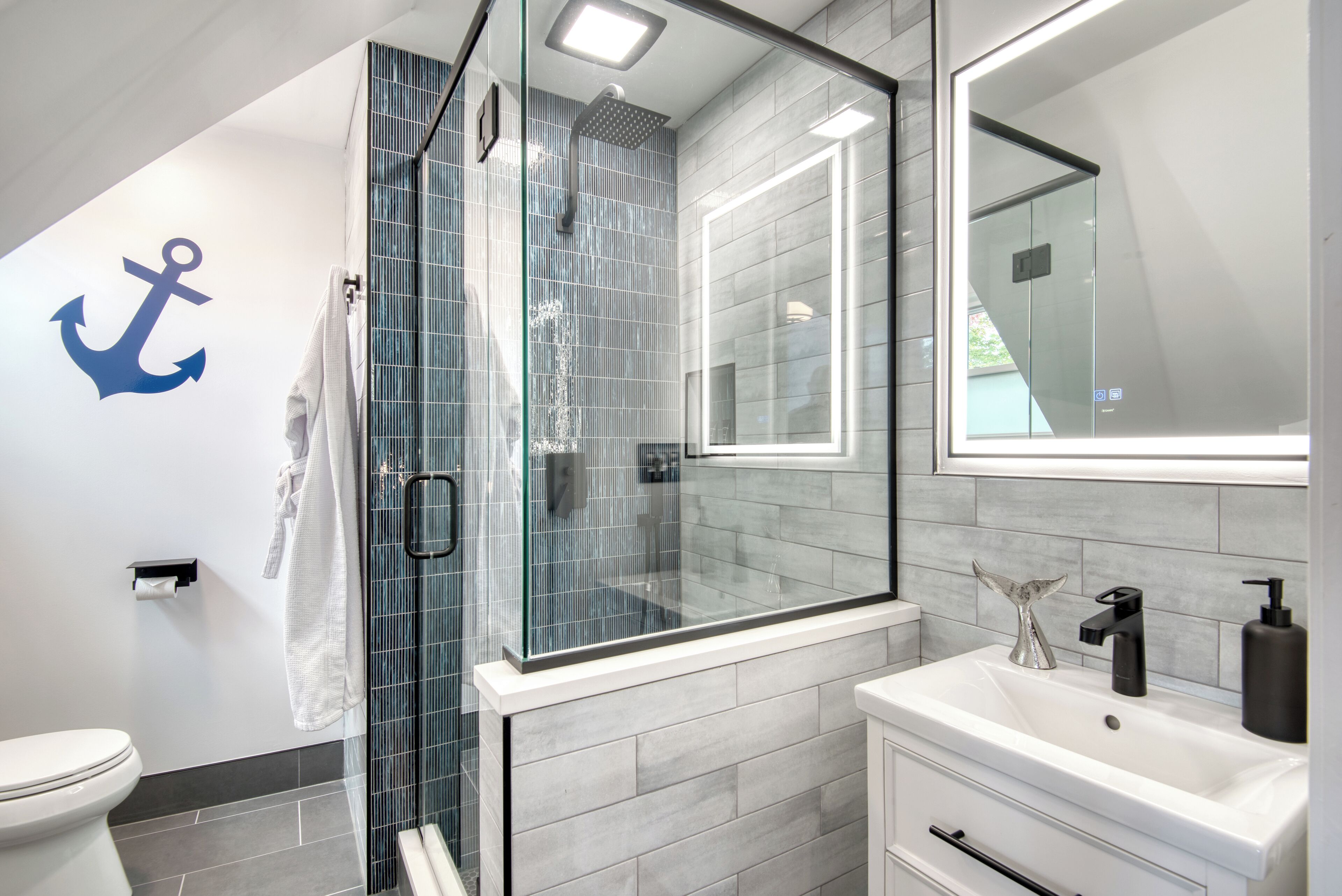 A modern bathroom with a glass shower enclosure, a white sink with a black faucet, and a large mirror above the sink.