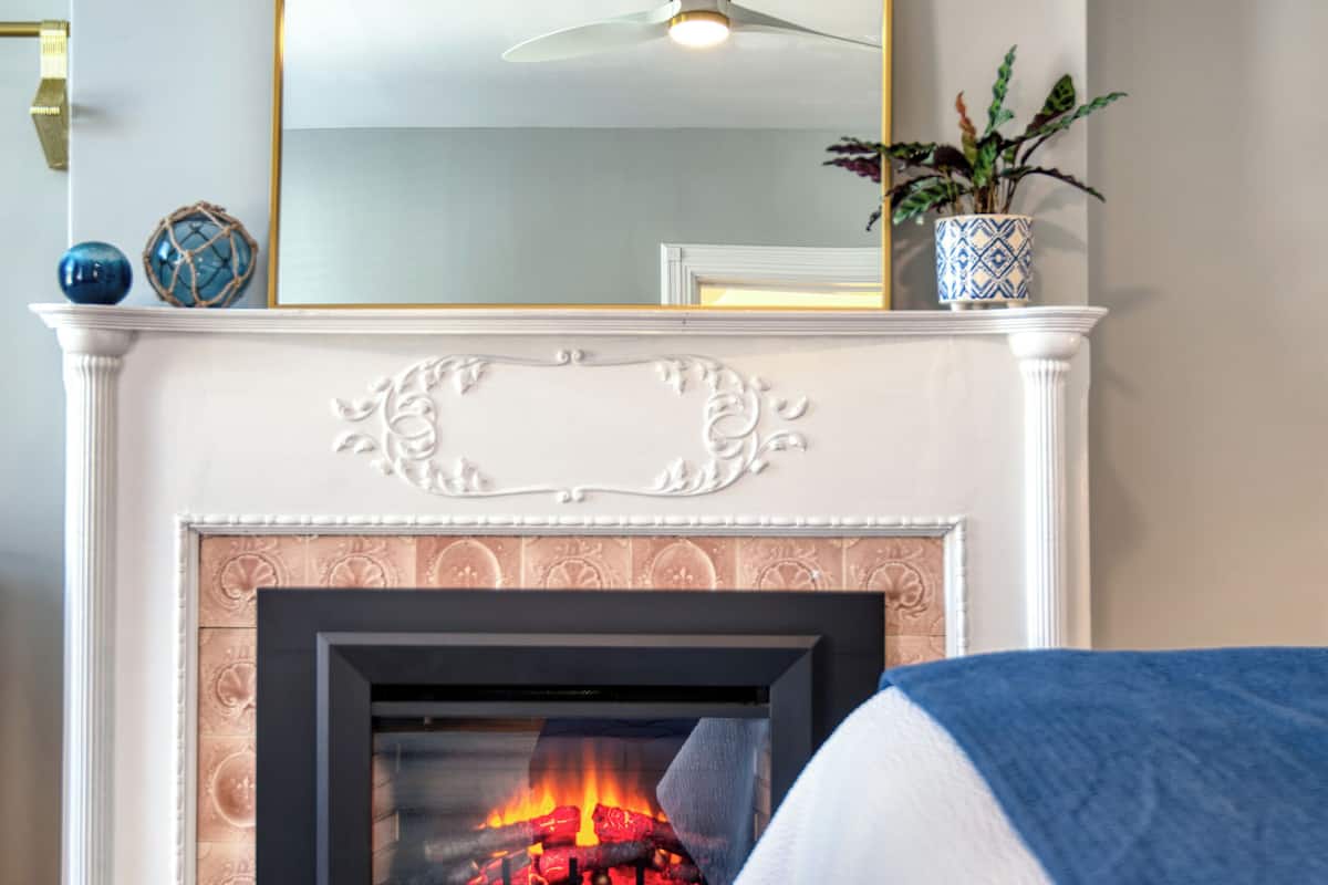 A room with a fireplace, a blue upholstered bench, and a mirror with a gold frame.