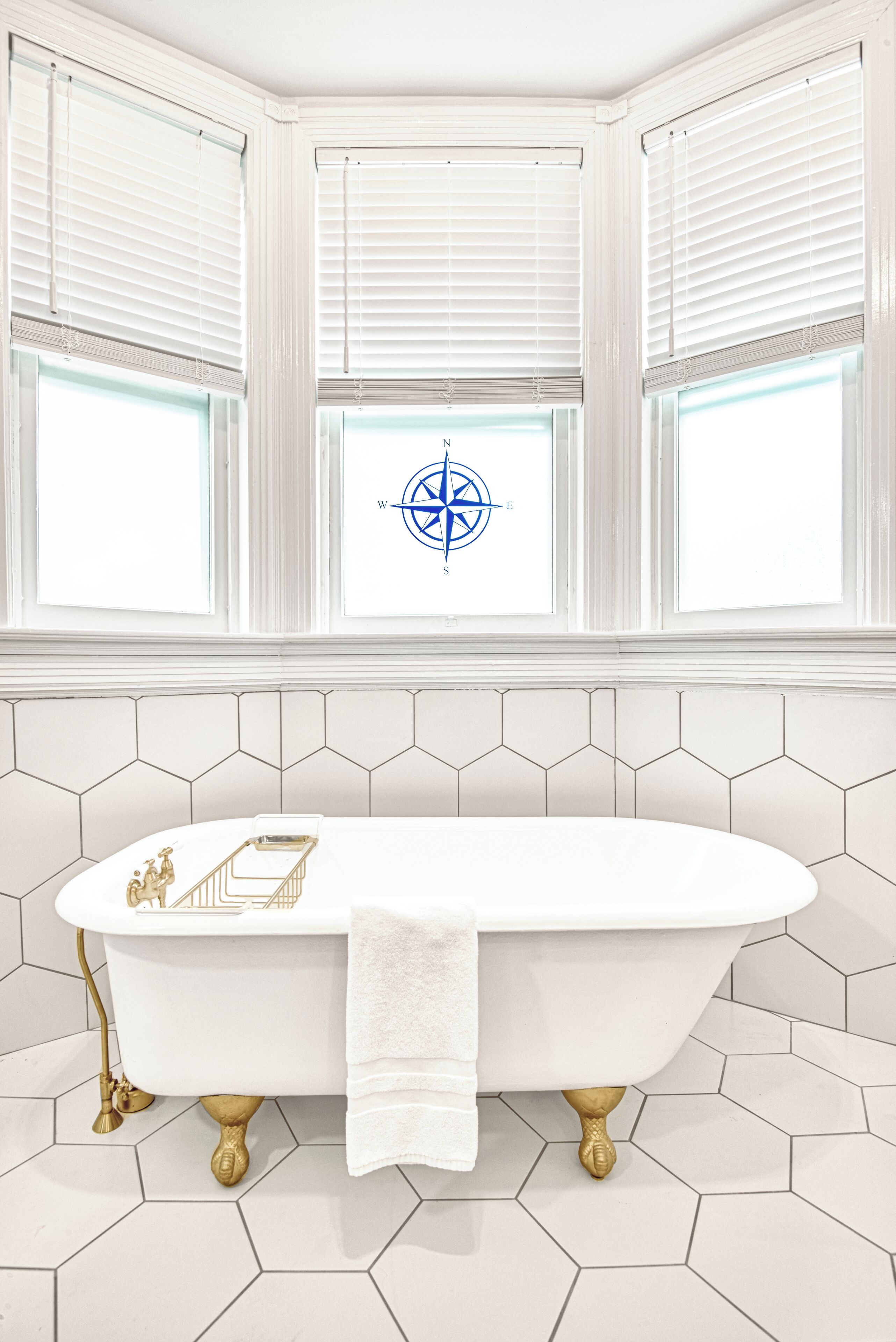 Un baño con bañera independiente, azulejos hexagonales blancos y una decoración de brújula en la pared.