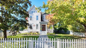 A two-story house with a front porch, a picket fence, and a well-maintained lawn. - Hudson Navigator (Hudson)