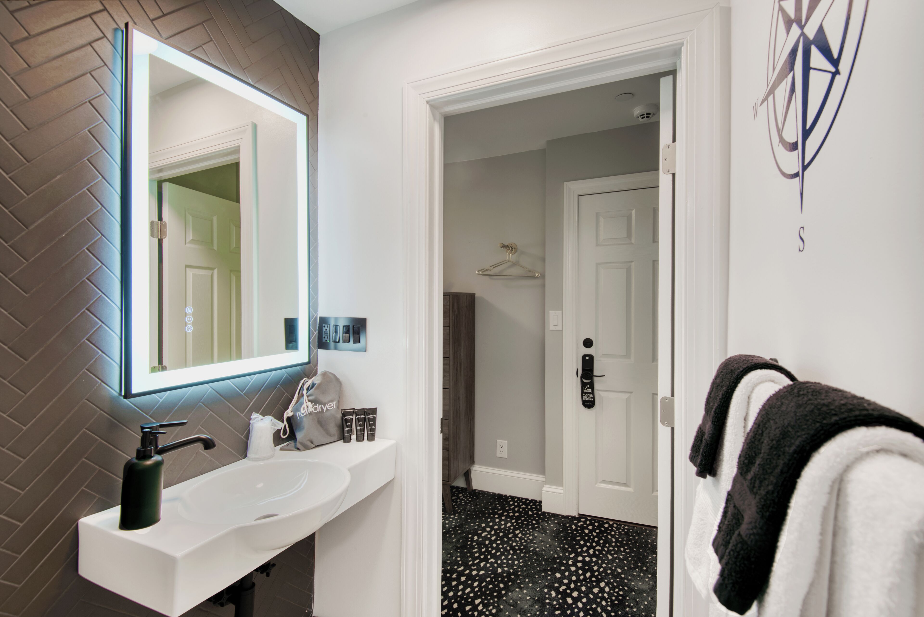 A bathroom with a white sink, black and white patterned floor, and a mirror with a lighted frame.