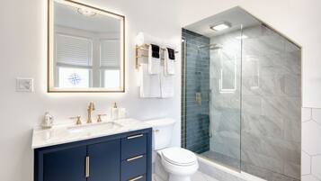 Un baño moderno con ducha envuelta en vidrio, inodoro blanco y tocador azul oscuro con detalles dorados.