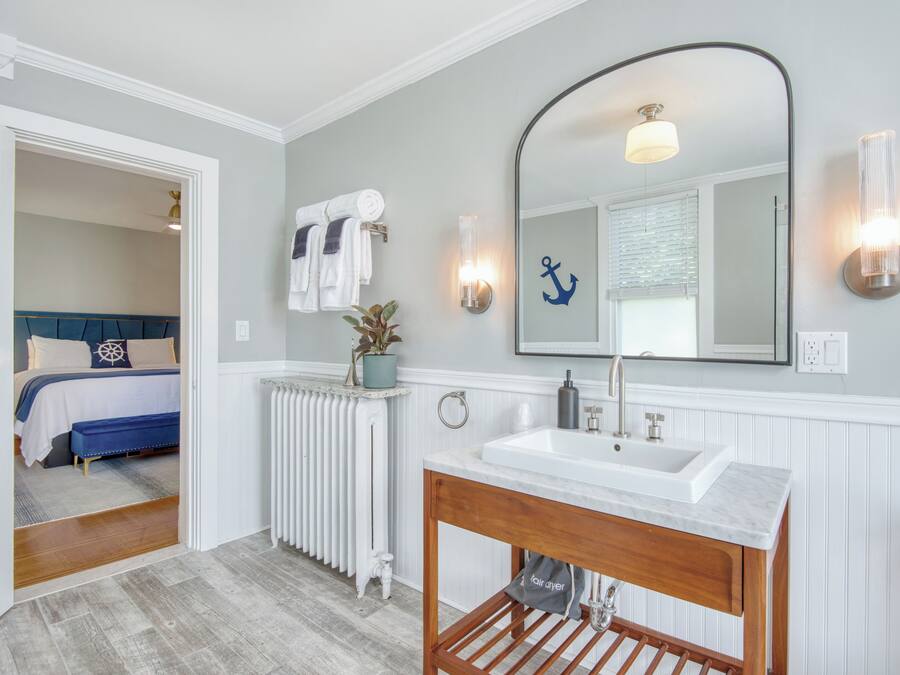 A bathroom with a white sink, wooden vanity, and a large mirror. There is a towel rack with towels and a potted plant on the radiator.