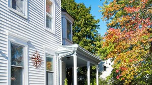 A two-story house with a porch, a white picket fence, and a garden with various plants and flowers. - Hudson Navigator (Hudson)