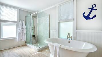 Un baño moderno con ducha envuelta en vidrio, una bañera independiente y un amplio ventanal con persianas.