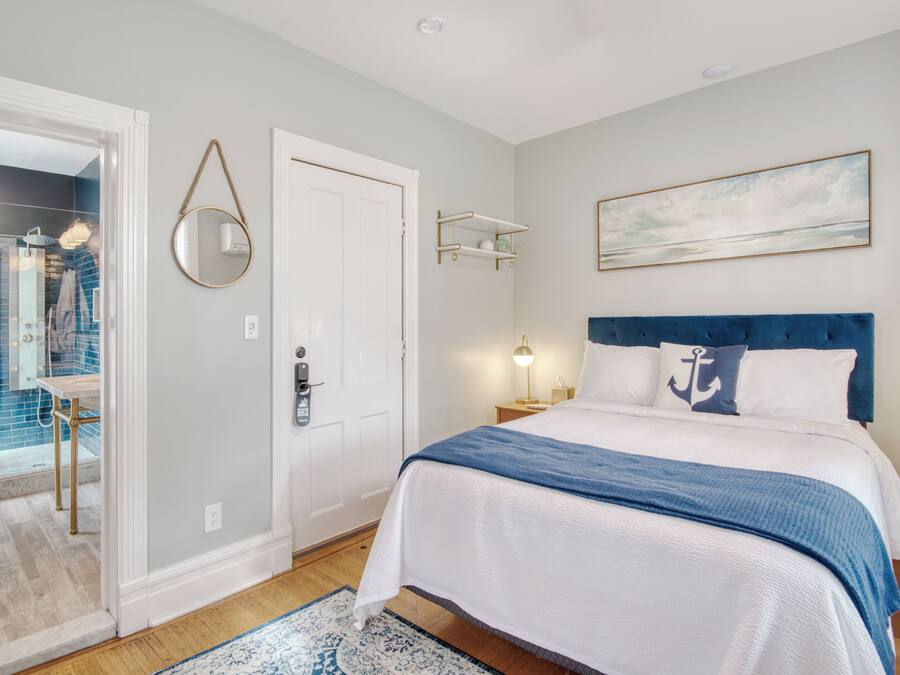 Quarto com cama, porta, prateleira na parede e um quadro.