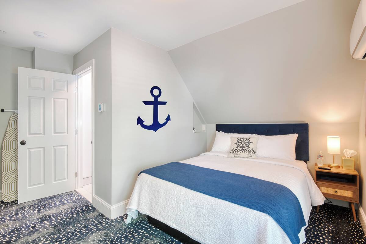 A bedroom with a bed, a nightstand, a wall-mounted anchor decoration, a door, and patterned flooring.
