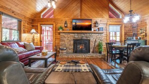 L’intérieur d’un chalet confortable, avec des murs en rondins de bois, une cheminée en pierre, des meubles en cuir et un coin repas.