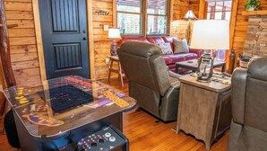 Une pièce confortable, aménagée comme un chalet, avec un intérieur en bois, un canapé en cuir rouge, une table de jeux et une cheminée en pierre.