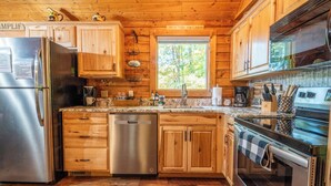 Une cuisine de style rustique, avec des meubles en bois, un réfrigérateur en acier inoxydable, un lave-vaisselle, une cuisinière et une fenêtre donnant sur les arbres.