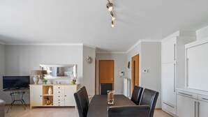 A modern kitchen with white cabinets, a dining table with black chairs, and a TV on a small table. - Beautiful Flat in the Centre of Blankenberge (Blankenberge)
