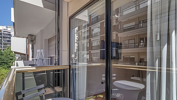 A modern apartment with a balcony, a glass door leading to a bathroom, and a view of neighboring buildings. - Comfy Studio in Recoleta with Pool & Gym (Buenos Aires)