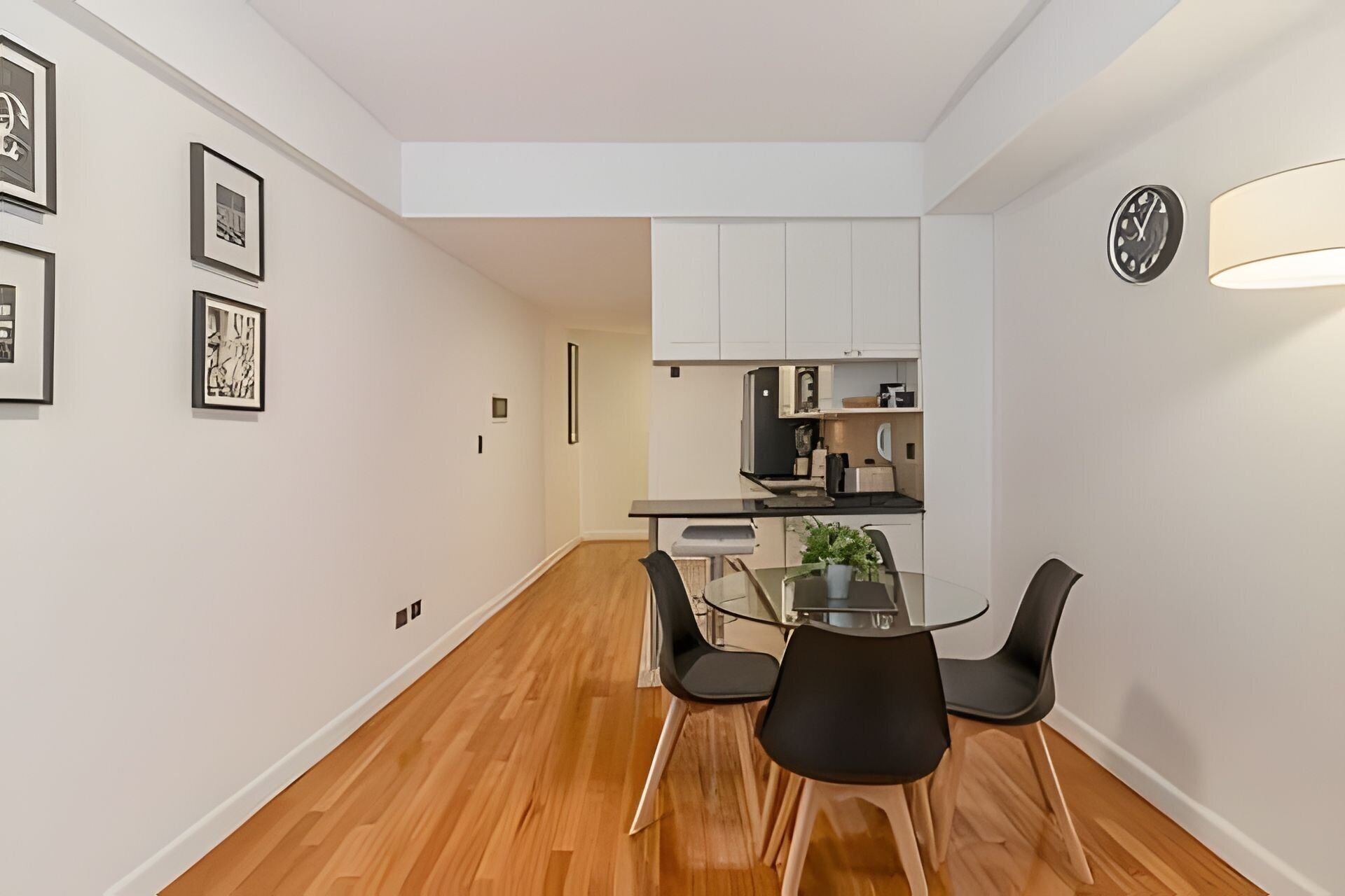 Een moderne keuken met witte kasten, een zwart aanrecht en een glazen eettafel met zwarte stoelen.