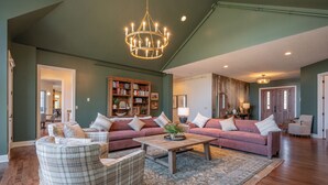 A spacious living room with a large chandelier, a fireplace, and a bookshelf filled with books. - Cozy Lake Retreat w/ Dock, Fire Pit & Views (Oakland)