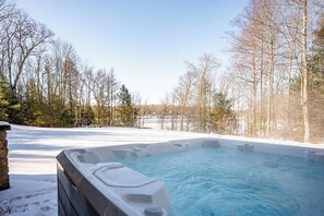 Un bain à remous entouré de terre enneigée et d’arbres sans feuilles.