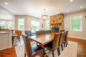 A spacious dining area with a long wooden table and leather chairs, a stone accent wall, and a chandelier.