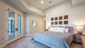 A bedroom with a large bed, a sliding glass door, a mirror, and a wall with wooden art pieces. - Cozy Lake Retreat w/ Dock, Fire Pit & Views (Oakland)