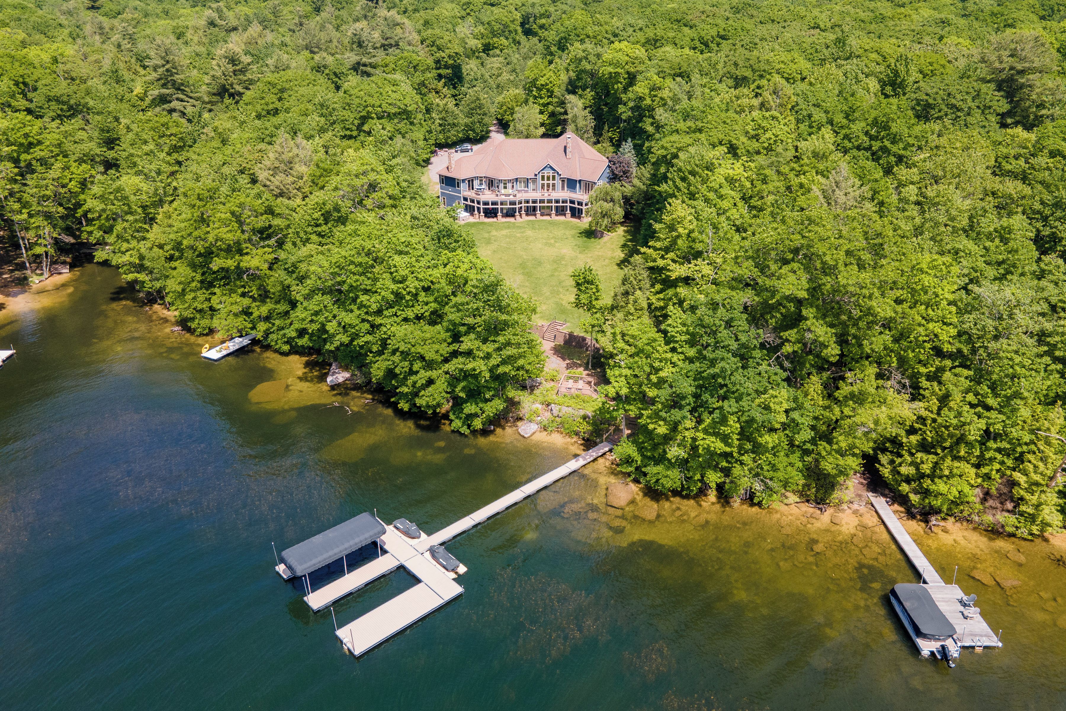 A large house surrounded by dense forest, a dock, and a small boat.