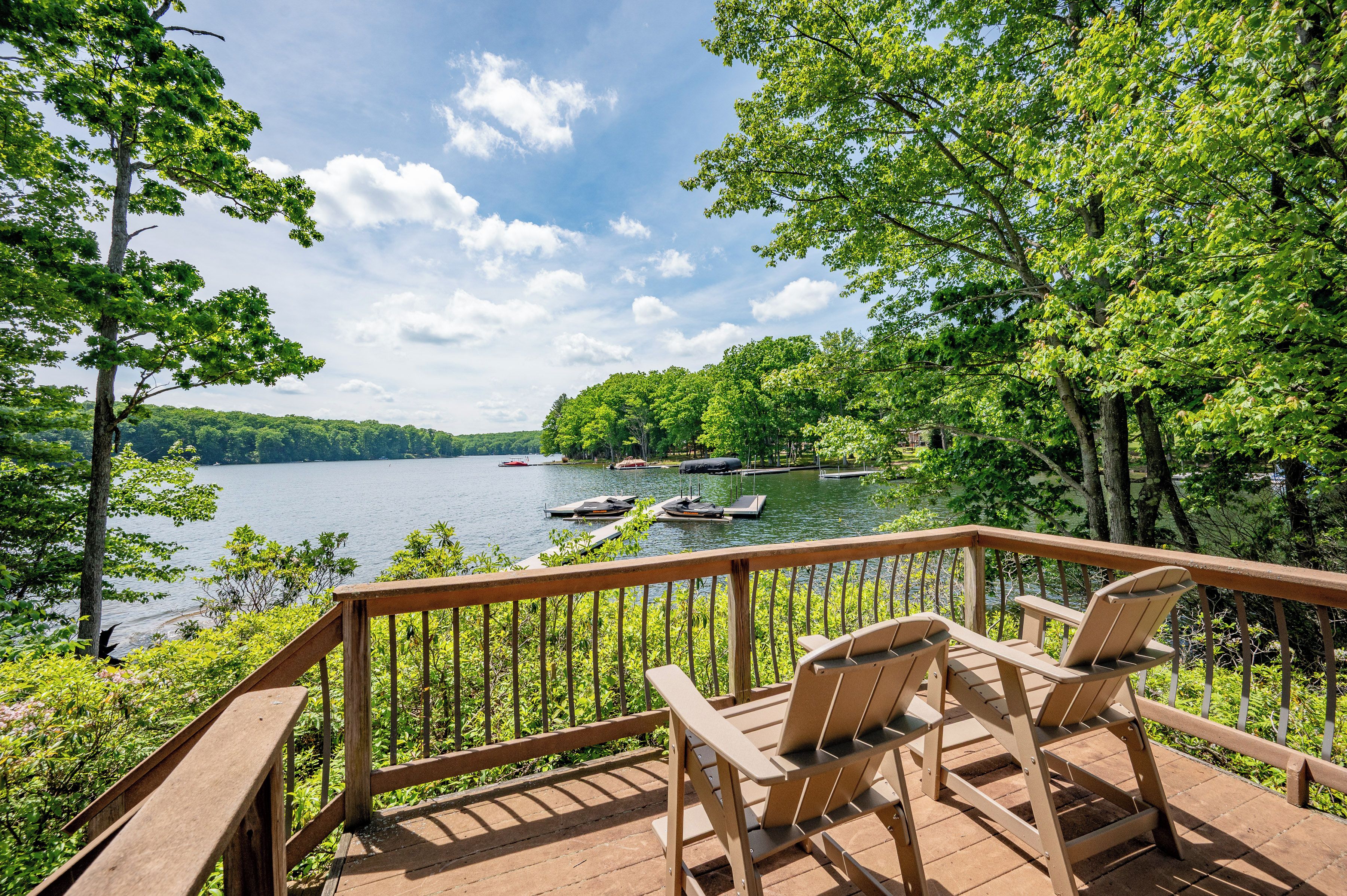 A wooden deck with chairs overlooking a lake with boats, surrounded by trees.
