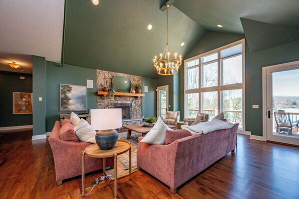 A spacious living room with a fireplace, large windows, and a chandelier. - Cozy Lake Retreat w/ Dock, Fire Pit & Views (Oakland)