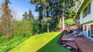 Un jardin avec une terrasse en bois, une pelouse et une maison dotée d’un porche abrité.