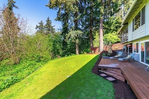 A backyard with a wooden deck, a lawn, and a house with a covered porch.